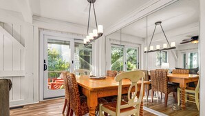 A dining area with a wooden table and chairs, a chandelier, and a view through glass doors. - Beautiful sunsets at this marsh view condo; enjoy the community pool close to all islands amenities (Bald Head Island)