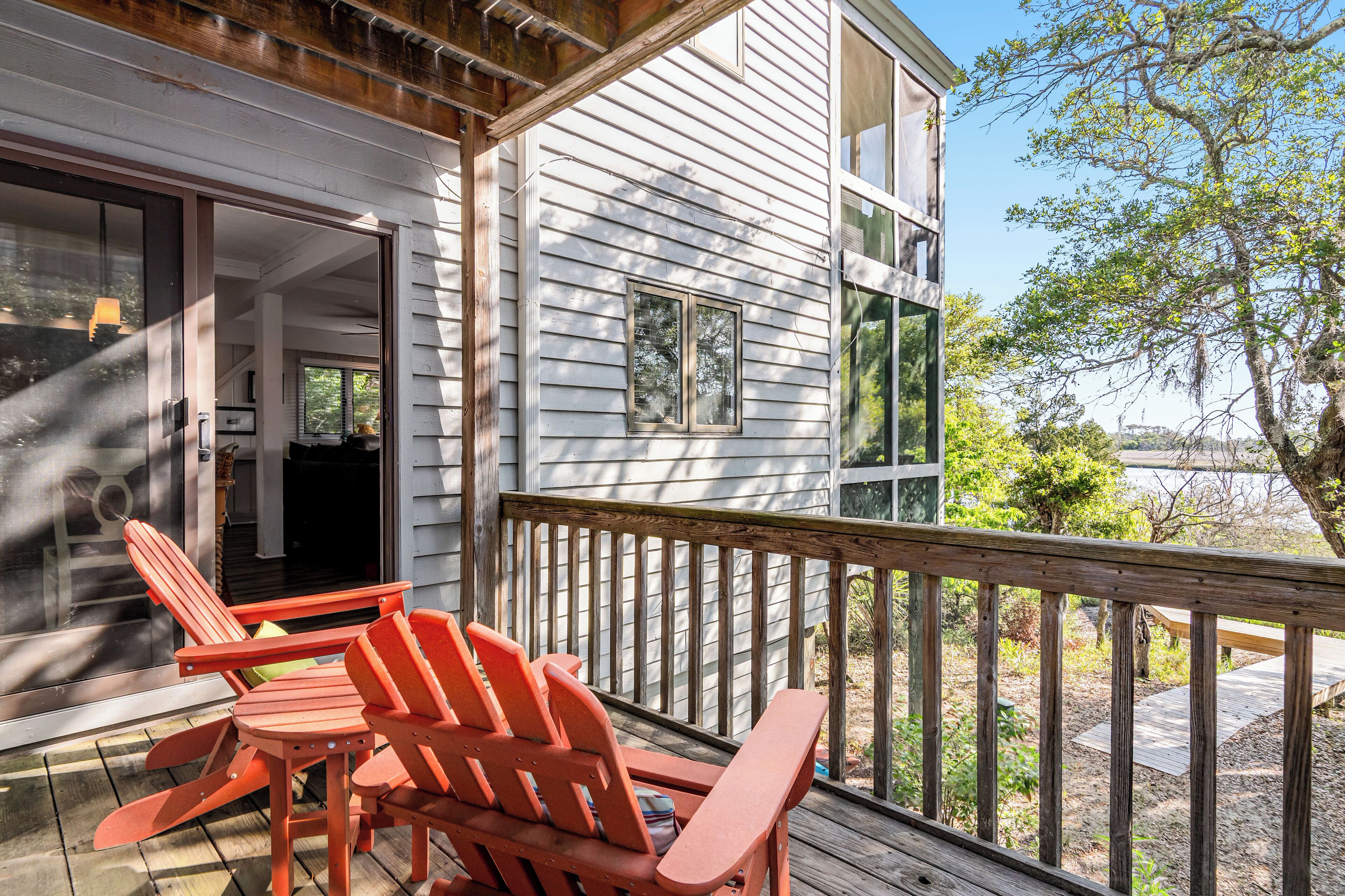 A wooden deck with red Adirondack chairs, a wooden railing, and a view of a white building with a large window and a door.