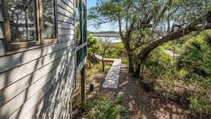 A wooden cabin with a deck leading to a natural area with trees and a view of a lake. - Beautiful sunsets at this marsh view condo; enjoy the community pool close to all islands amenities (Bald Head Island)
