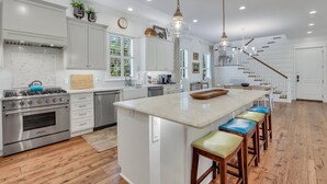 A spacious kitchen with a central island, stainless steel appliances, and a staircase leading to another level. - Magnificent East Beach Home! Heated Pool, 5BR/5.5BA Sleeps 16 (St. Simons Island)