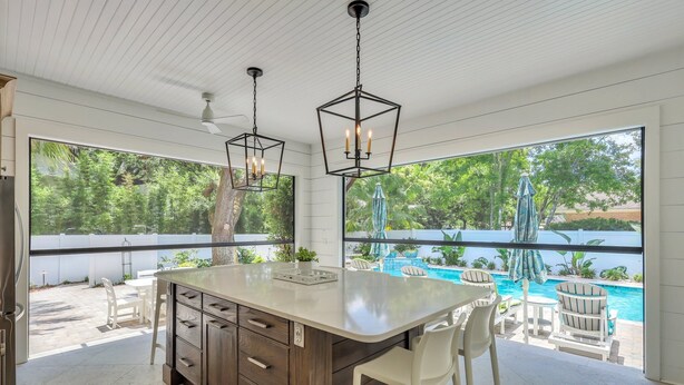 A spacious kitchen with a large island, pendant lighting, and a view of a swimming pool. - Magnificent East Beach Home! Heated Pool, 5BR/5.5BA Sleeps 16 (St. Simons Island)