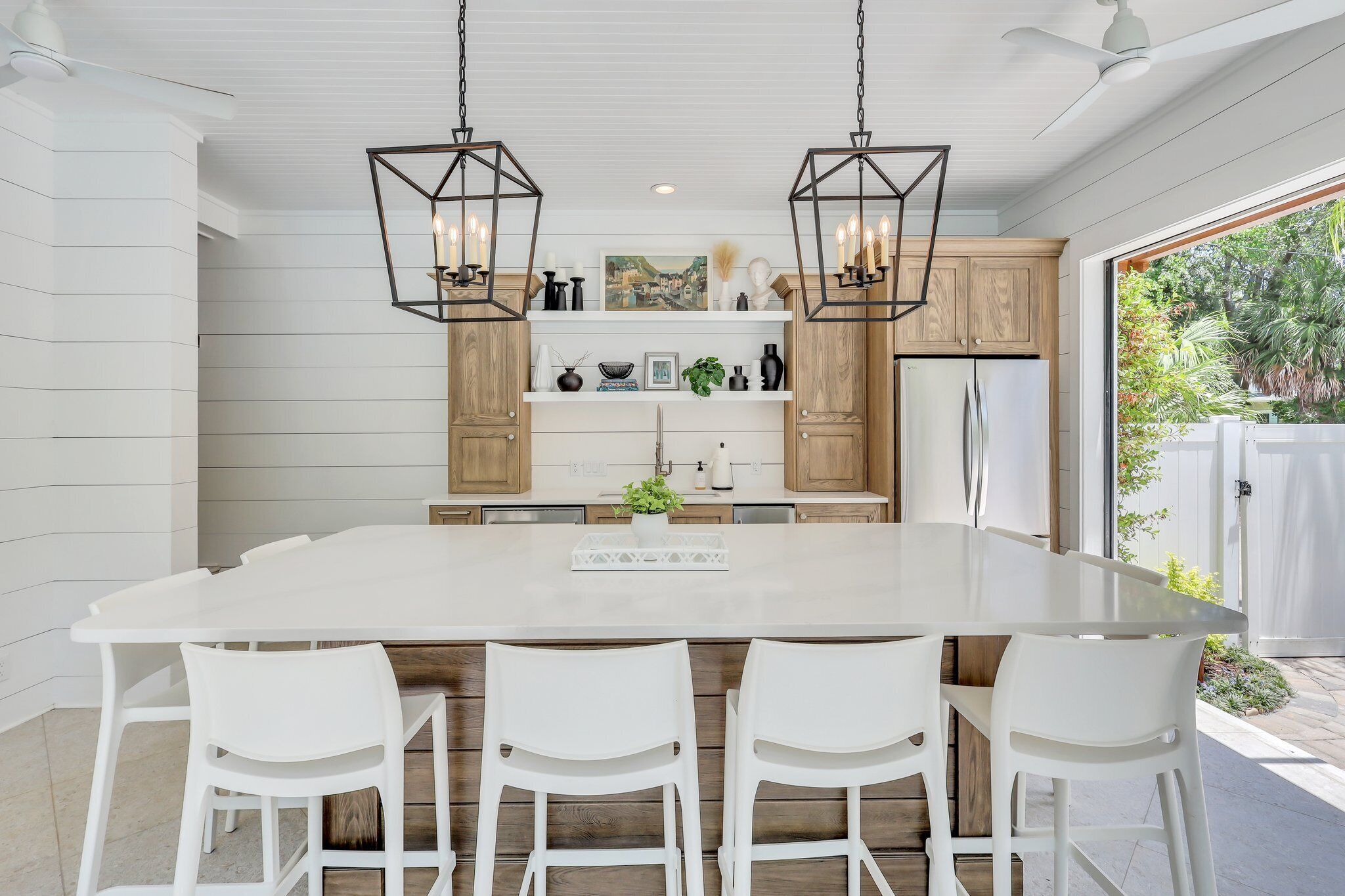A modern kitchen with a large island, white chairs, wooden cabinets, and pendant lighting. - Magnificent East Beach Home! Heated Pool, 5BR/5.5BA Sleeps 16 (St. Simons Island)