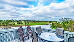 A deck with a table and chairs overlooking a golf course and a body of water.