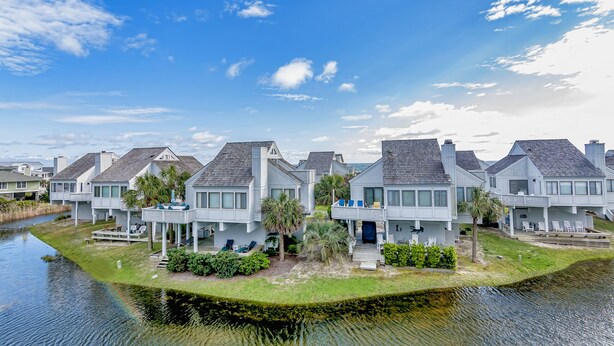 A row of modern houses with a canal in the foreground, featuring balconies and outdoor seating areas.