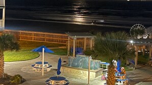 Vista notturna di un resort sulla spiaggia con un pontile in legno, posti a sedere all'aperto e una ruota panoramica sullo sfondo.
