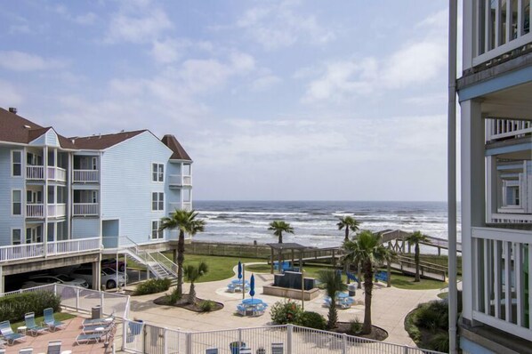 A beachfront hotel with multiple balconies, a pool area with sun loungers, and a view of the ocean.