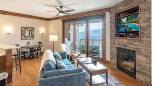Una sala de estar con chimenea de piedra, un televisor montado en la pared y vistas al exterior.