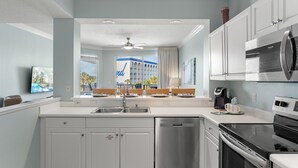 A modern kitchen with white cabinets, stainless steel appliances, and a large window offering a view of a building with blue accents.