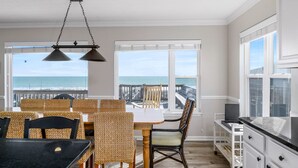 Un espace repas offrant une vue sur l’océan, comprenant une table et des chaises, un luminaire suspendu et une fenêtre donnant sur la jetée.