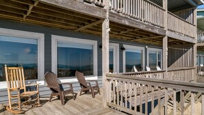 Une terrasse en bois avec deux fauteuils à bascule et une table, donnant sur une plage.