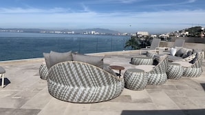 Eine Terrasse mit Korbmöbeln und Blick auf das Meer und die Skyline der Stadt.