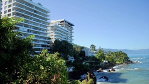 Ein Hotel an der Küste mit mehreren Balkonen, üppiger Bepflanzung und Blick aufs Meer.