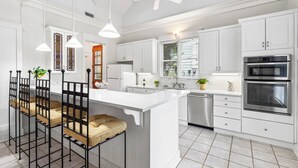 Een moderne keuken met witte kasten, een groot eiland, roestvrijstalen apparatuur en een plafondventilator.