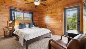 Un dormitorio de cabaña de madera con cama, escritorio, silla, ventilador de techo y ventana.