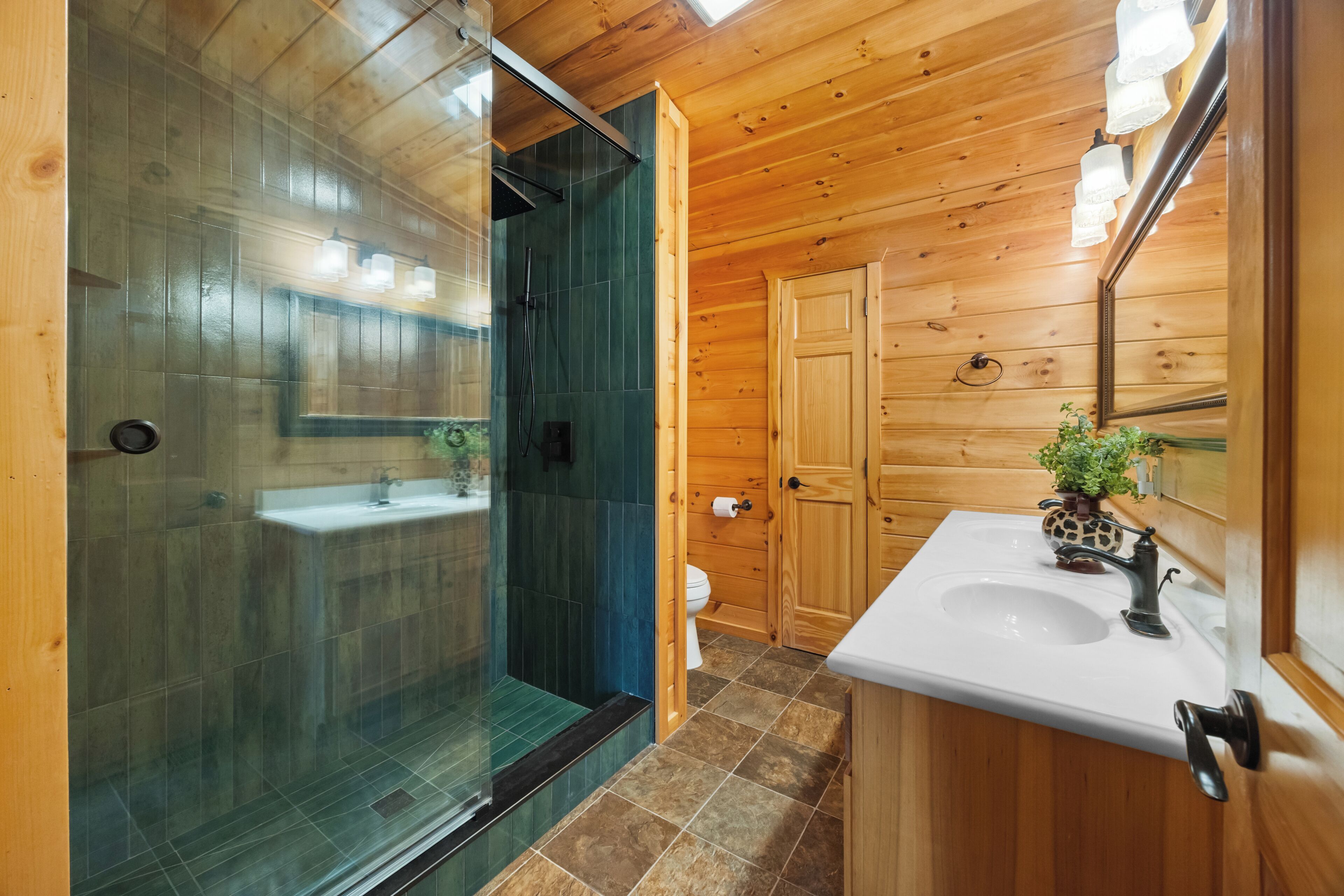 Une salle de bain rustique, avec des murs en bois, une douche en verre, un lavabo et des toilettes.