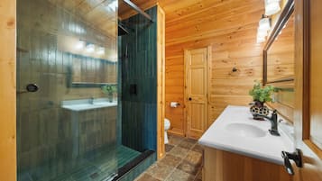 Une salle de bain rustique, avec des murs en bois, une douche en verre, un lavabo et des toilettes.