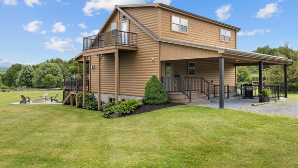 Eine zweistöckige Holzhütte mit Balkon, überdachter Veranda und gepflegtem Rasen.
