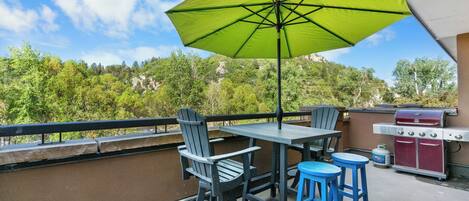 Un patio al aire libre con una mesa, sillas, un paraguas verde y una parrilla.
