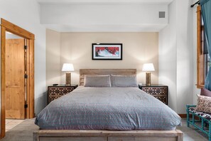 Une chambre à coucher avec un lit en bois, deux tables de chevet avec des lampes, un tableau encadré au mur et une porte en bois.
