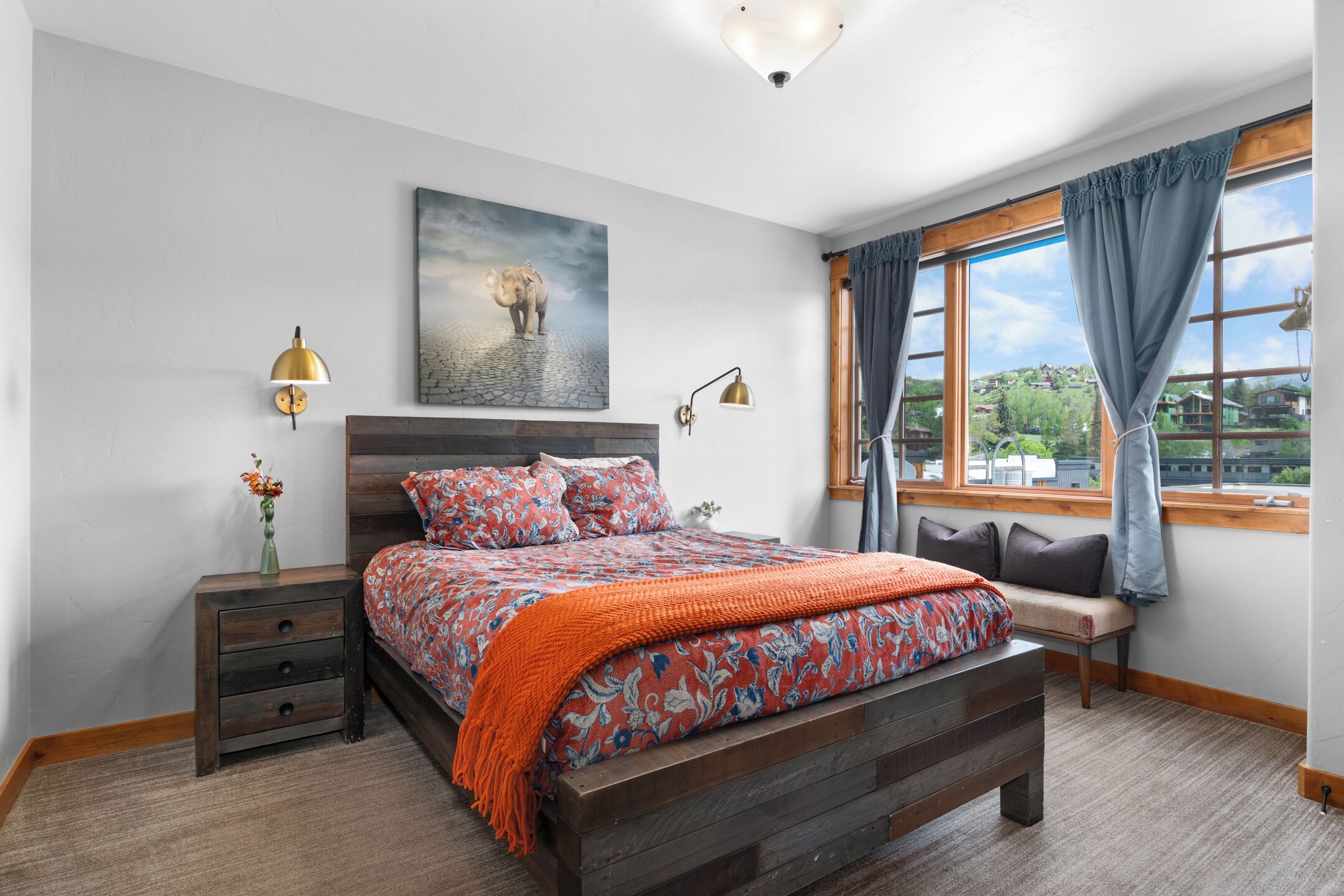 Une chambre à coucher avec un grand lit, une table de chevet, un banc près de la fenêtre et un tableau au mur.