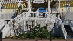 A multi-story building with a sign reading "Beach Club" and a white staircase leading to the entrance. - Beachfront at Pointe West. Walk to the beach and the club all just steps away! (Galveston)