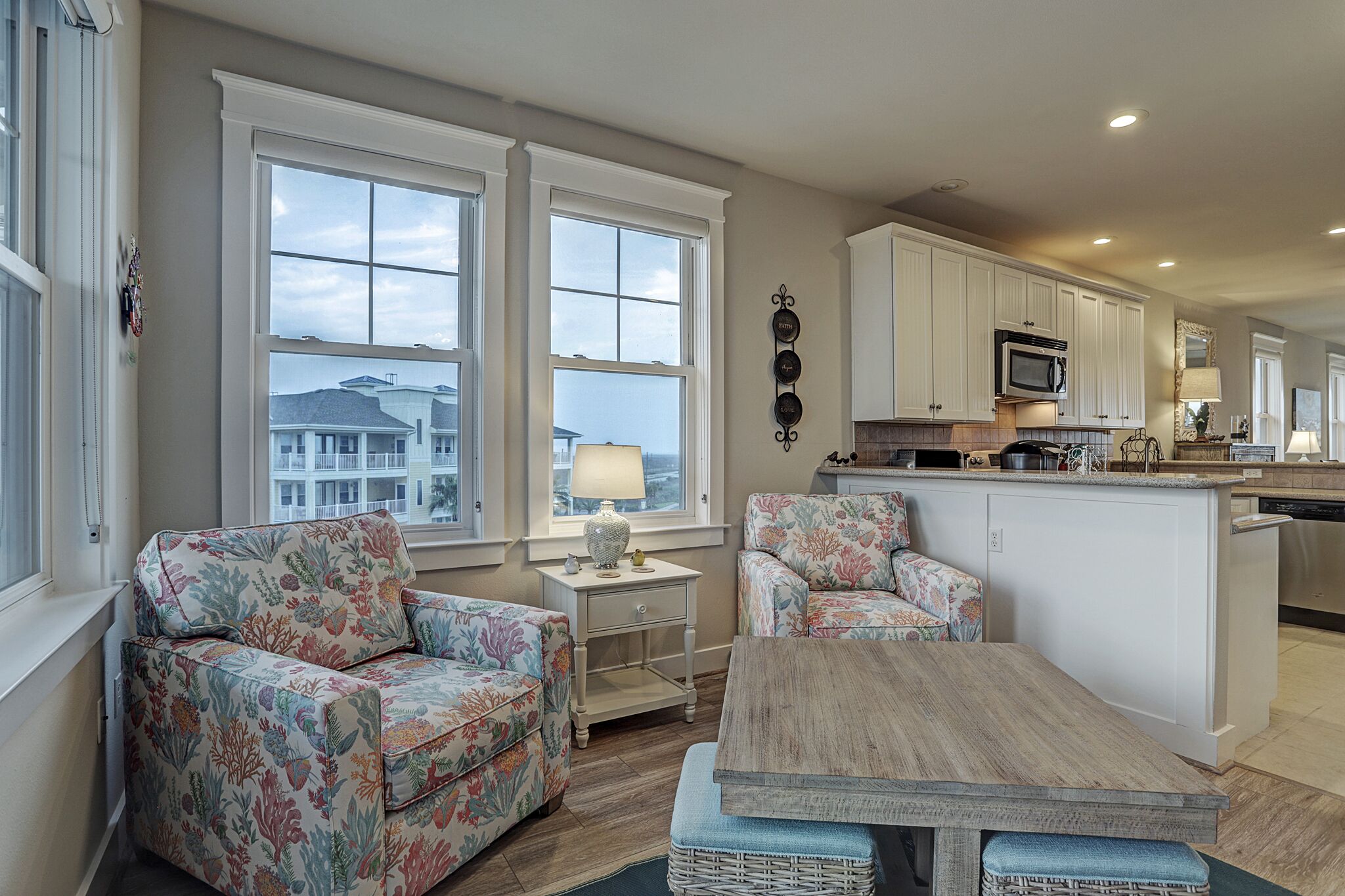 A spacious living area with two large windows, a kitchen with white cabinets, and a central island.