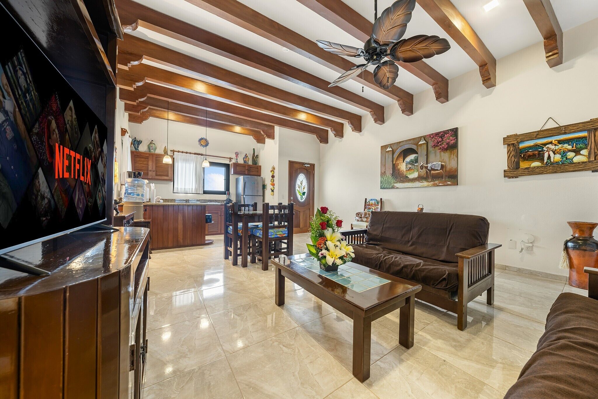 Amplia sala de estar con techo de madera, televisor, sofá, mesa de centro y cocina al fondo.