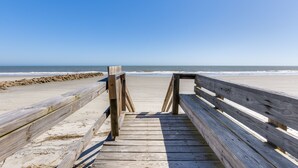 Un muelle de madera que conduce a una playa arenosa, con el océano al fondo.