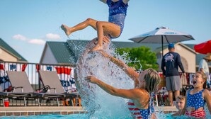 A poolside scene with a person performing a flip into the water, surrounded by onlookers.
