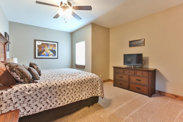 A bedroom with a bed, a dresser, a television, a ceiling fan, a window, and a framed picture on the wall.