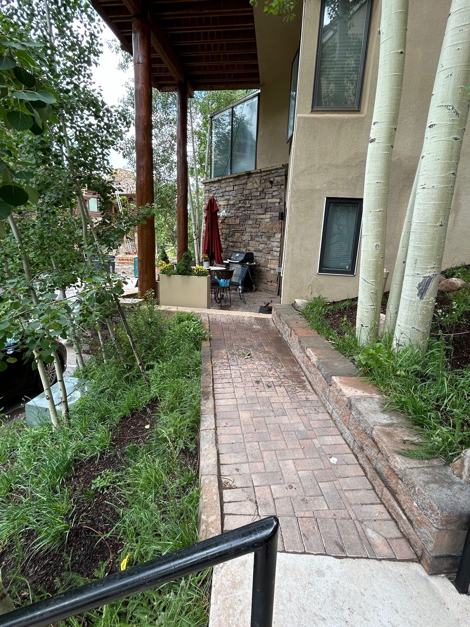 A covered patio with a brick pathway leading to a stone wall and a grill area.