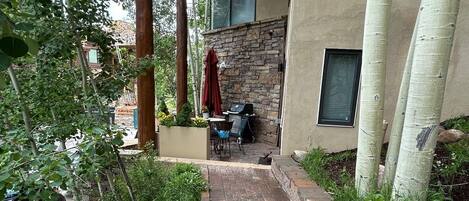 A covered patio with a brick pathway leading to a stone wall and a grill area.