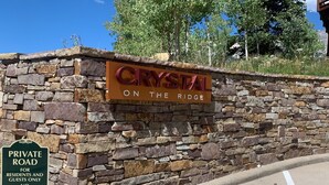 Un mur de pierre sur lequel est affiché un panneau indiquant « CRYSTAL ON THE RIDGE » et un autre panneau indiquant « CHEMIN PRIVÉ, RÉSERVÉ AUX RÉSIDENTS ET À LEURS INVITÉS, DÉFENSE D’Y PENÉTRER ».