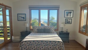 Un dormitorio con una cama grande, dos mesitas de noche, un ventanal con vistas y cuadros enmarcados en la pared.