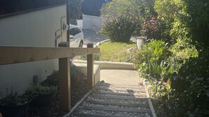Un sendero que lleva a una casa con porche, rodeada de vegetación y un cielo despejado.