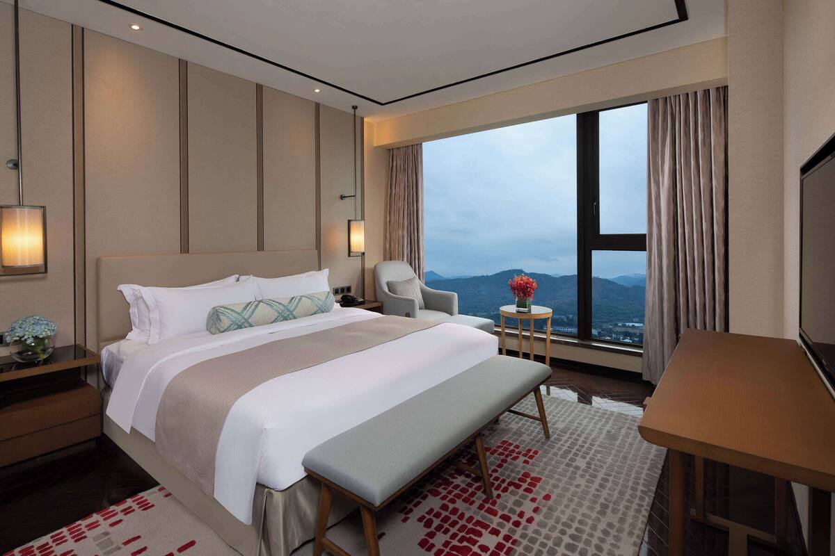Una habitación de hotel con una cama grande, un escritorio, una silla y vistas a las montañas a través de la ventana.