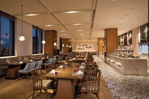 Een ruim restaurant met lange tafels, stoelen en een buffet.