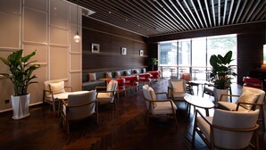 Un intérieur moderne avec des murs lambrissés en bois, un coin salon doté de canapés rouges et gris, et une grande fenêtre laissant entrer la lumière naturelle.