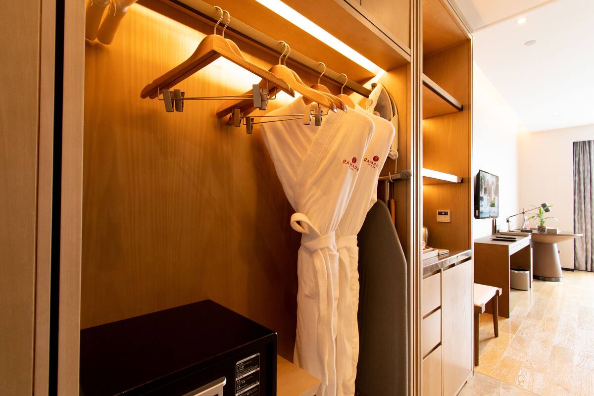 Habitación de hotel con pared de madera, televisor, escritorio y bata colgada en un perchero.