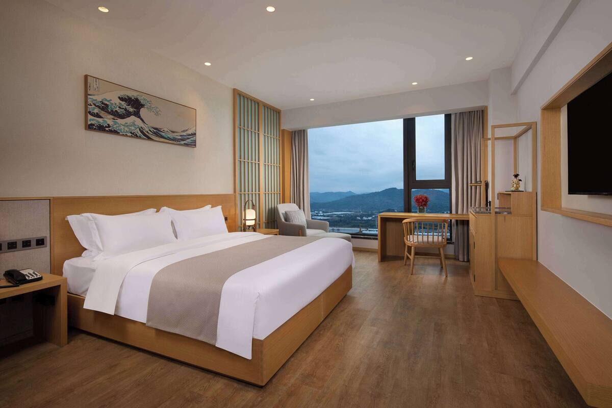 Habitación de hotel moderna con una cama grande, un escritorio, una silla y vistas de la ciudad.