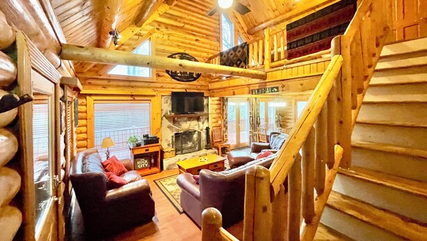 A log cabin interior with a fireplace, a television, and a cozy seating area.