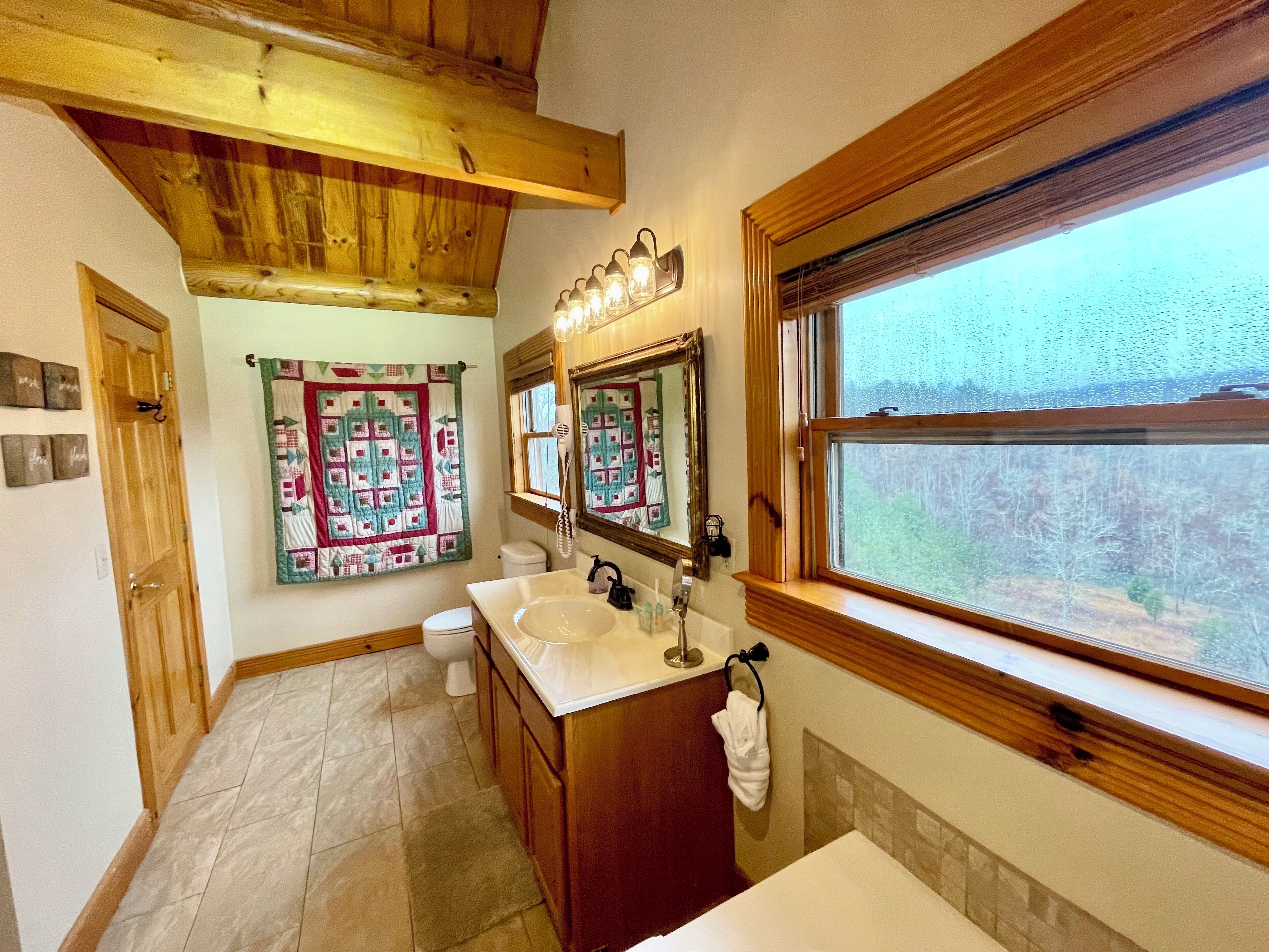 Een badkamer met een houten plafond, een groot raam, een wastafel en een toilet.