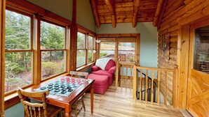 A cozy cabin interior with a wooden interior, a checkered game table, a red sofa, and a staircase.
