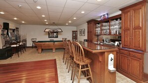 Une salle de billard équipée d’une table de billard, de chaises et d’un coin bar avec des meubles de rangement.