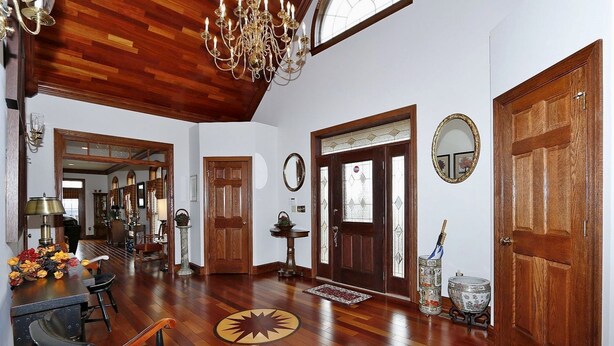 Un vaste salon doté d’un parquet en bois, d’un lustre, d’un coin repas avec une table et des chaises, et d’une grande porte en bois.