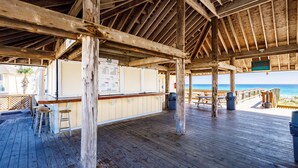 Une terrasse en bois avec un coin bar, des piliers en bois et une vue sur l’océan.