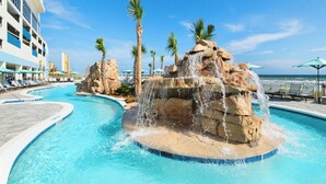 Una piscina con cascada, rodeada de palmeras y sillas de descanso.