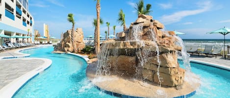 A swimming pool with a waterfall feature, surrounded by palm trees and lounge chairs.