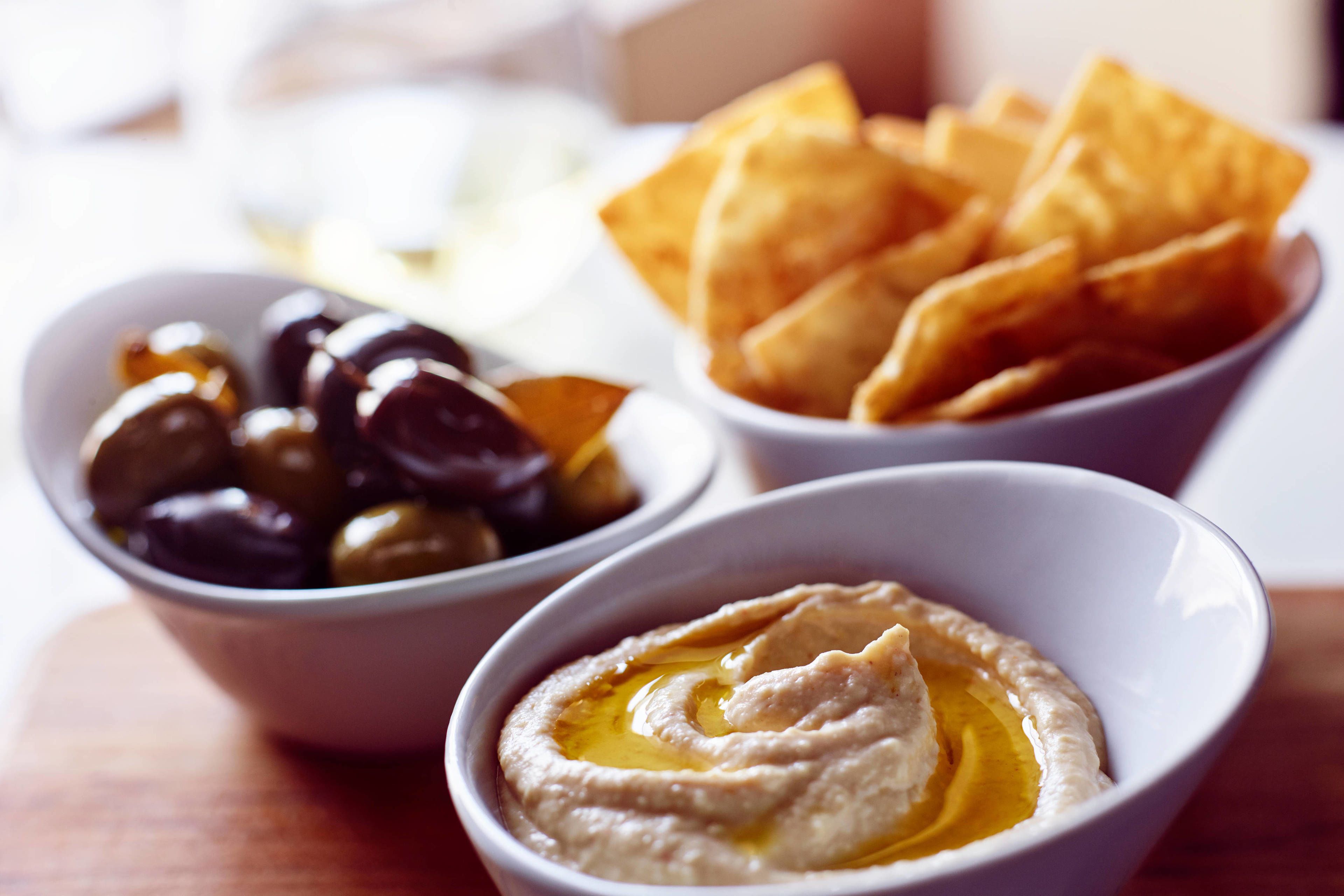 Drie schalen eten: één met olijven, één met hummus en één met chips.