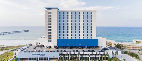 A hotel with a parking lot, a beach view, and a pier in the background.